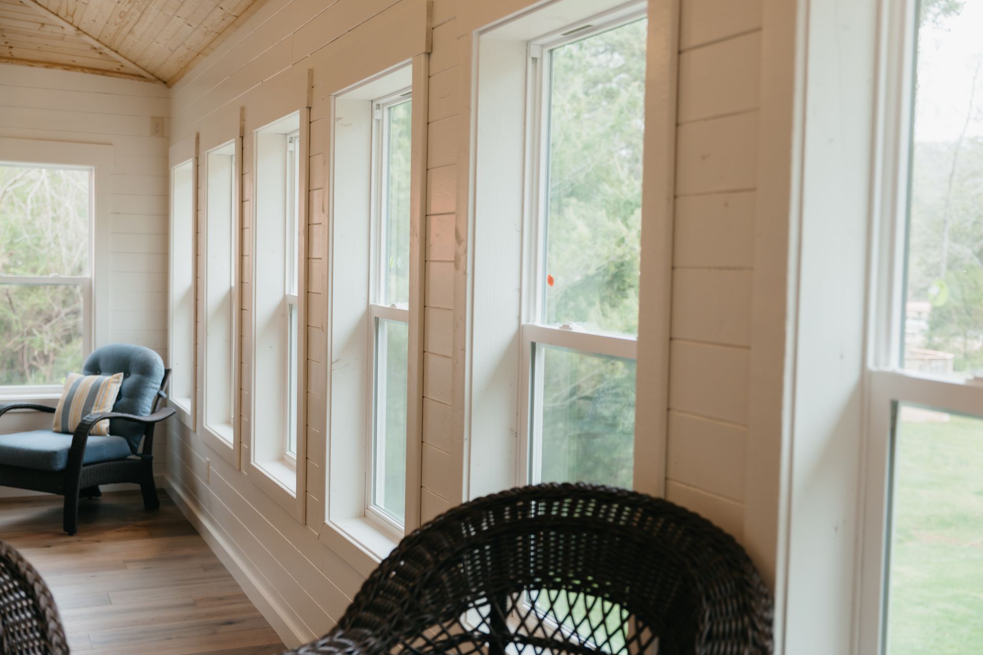 A sun room with wicker chairs and lots of windows.