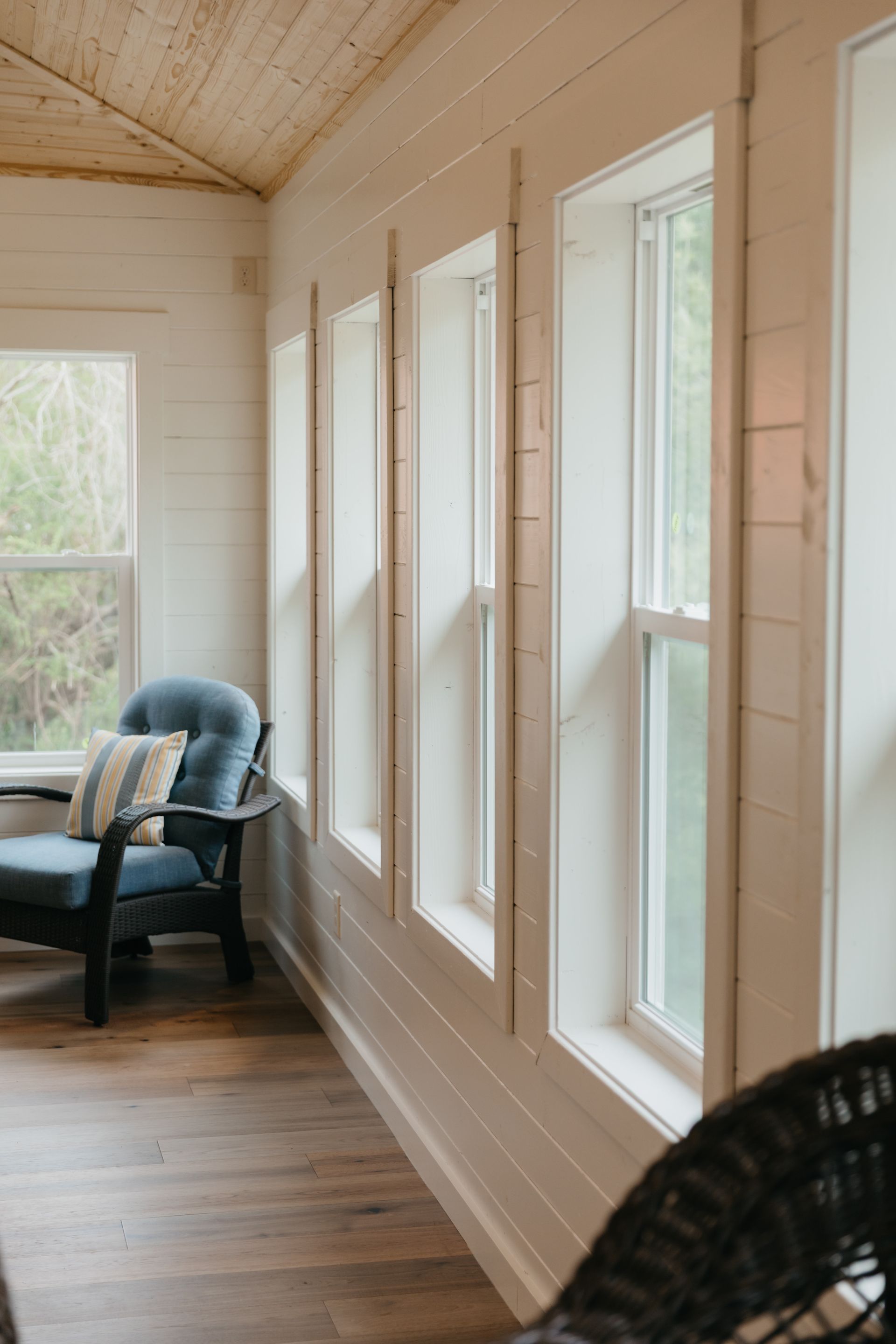 A living room with a chair and a table and lots of windows.
