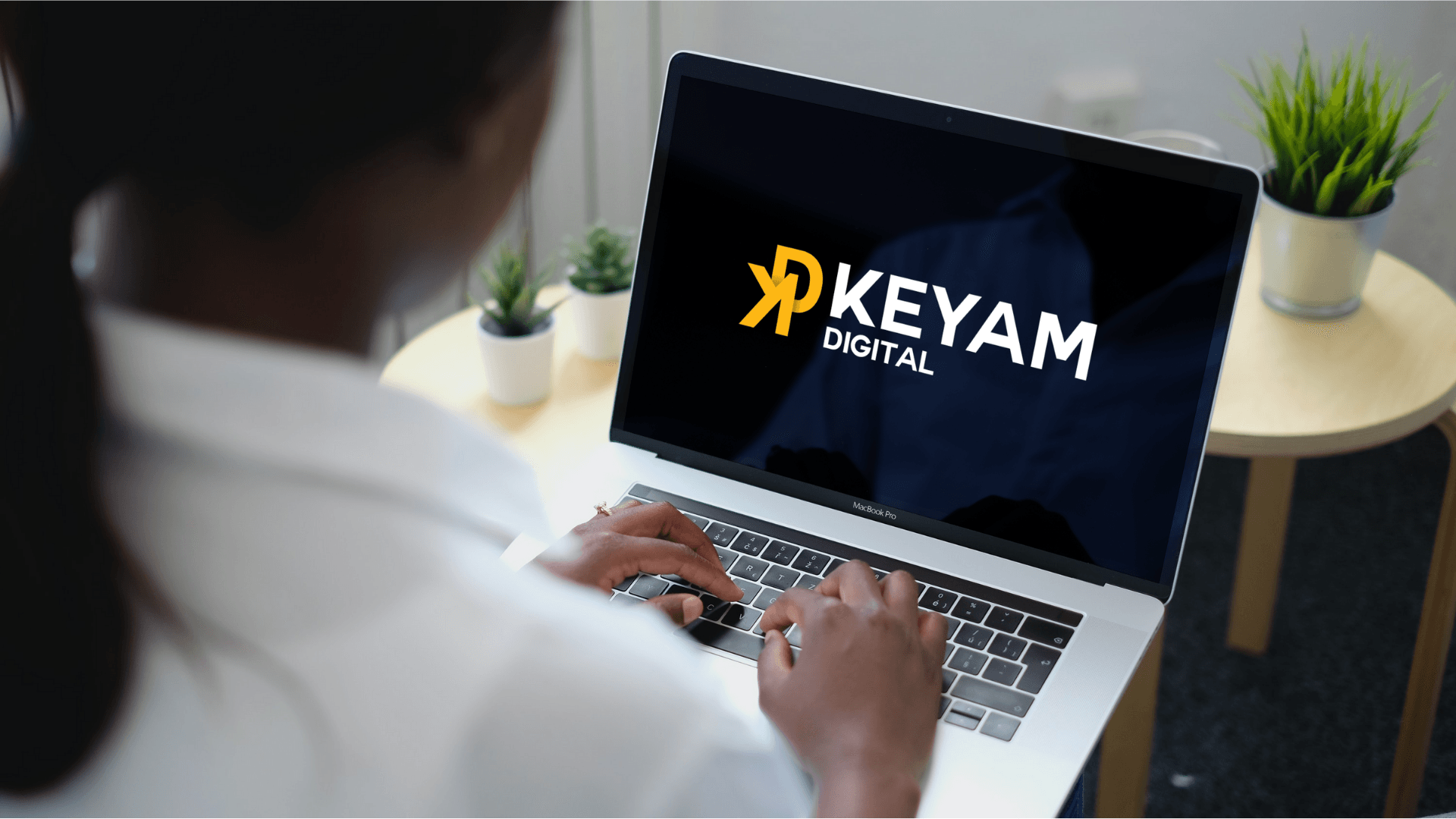 A woman is typing on a laptop with a keyam logo on the screen.
