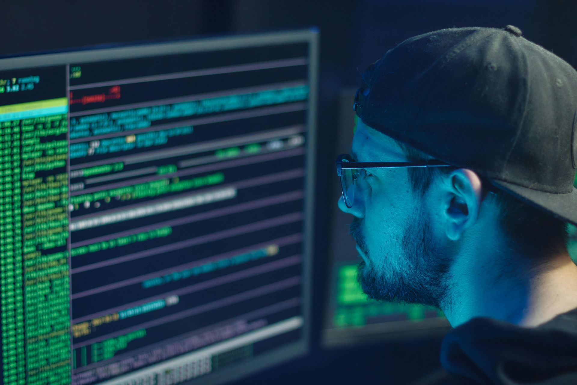 A man wearing a hat and glasses is looking at a computer screen.