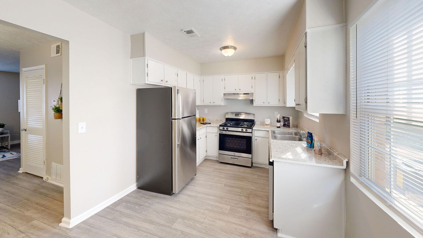 White kitchen with stainless steel appliances and light-colored flooring.