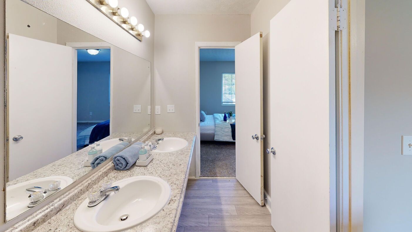 Bathroom with double sinks, large mirror, and doors leading to bedrooms. White walls, light counters.