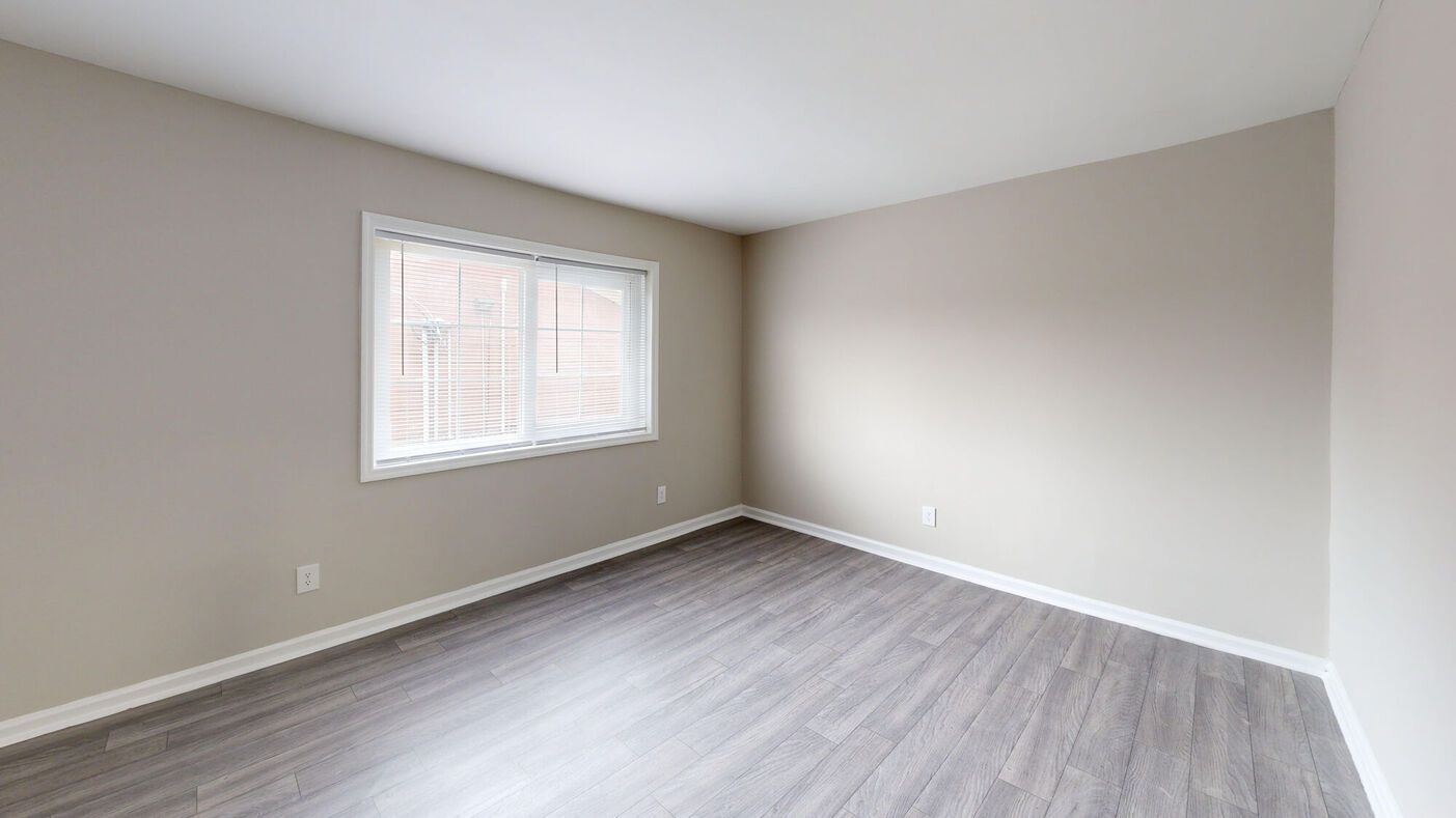 Empty room with gray wood-look floor, beige walls, and a window with blinds.