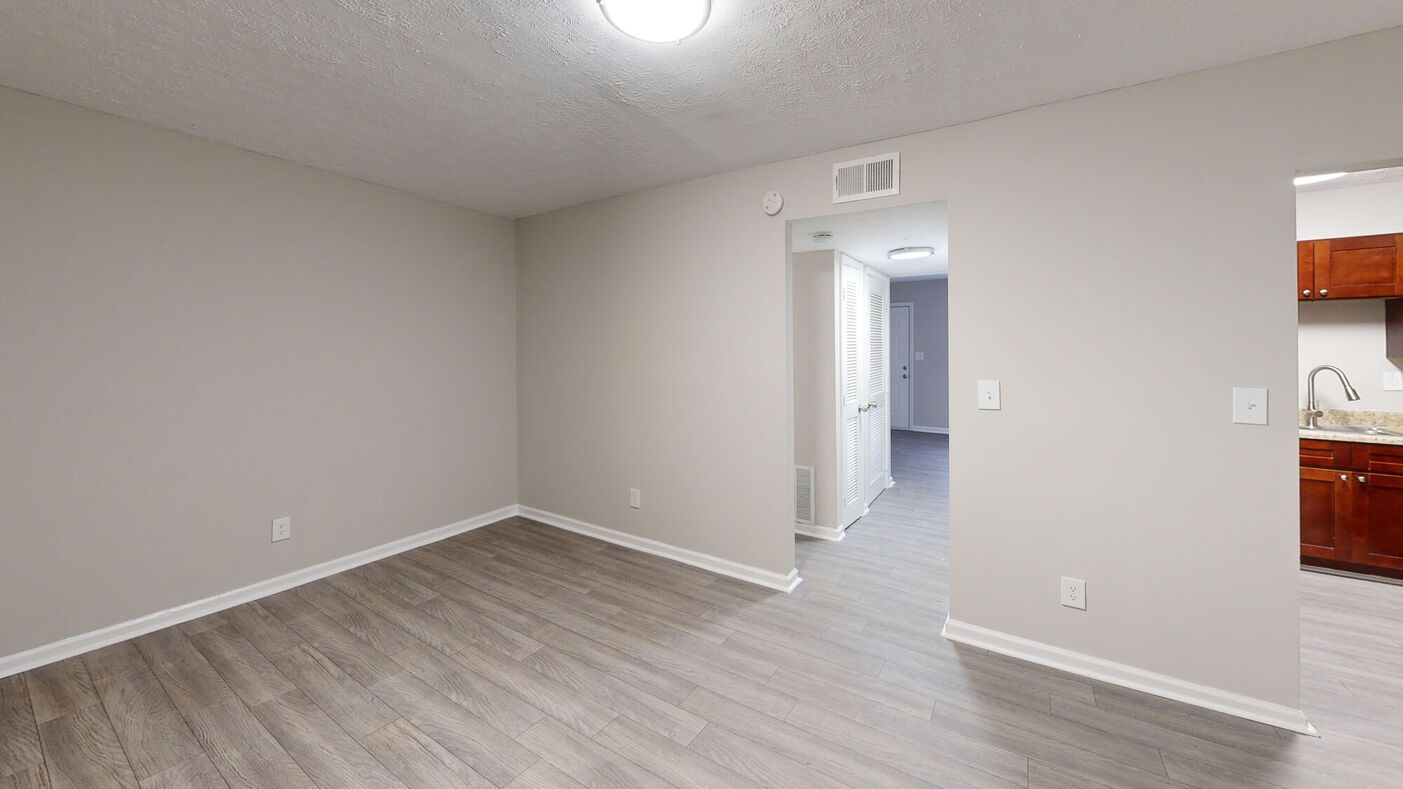 Empty apartment room with gray walls, wooden floor, and open doorways.