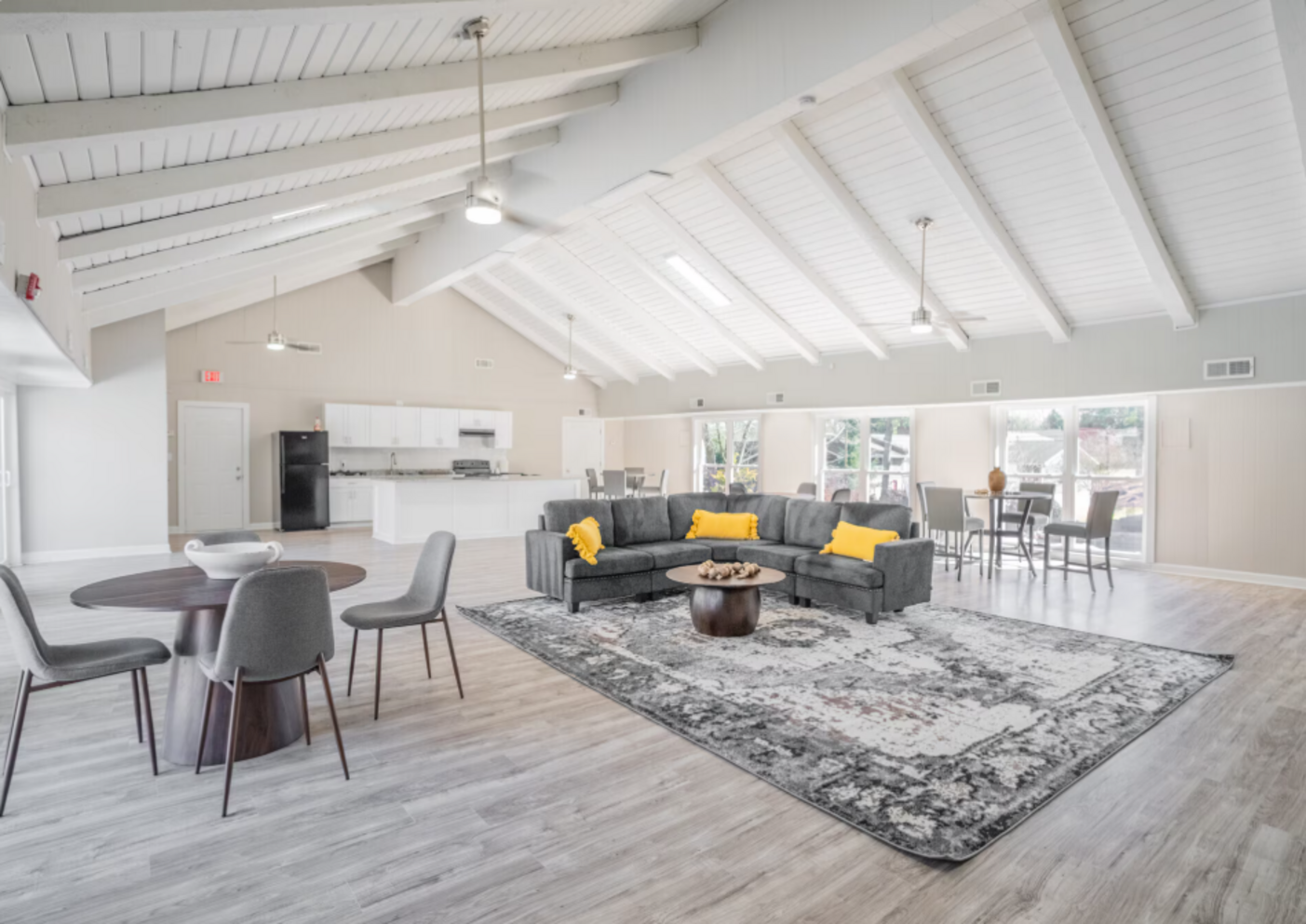 Spacious room with a gray sectional sofa, round tables, and high vaulted ceiling.