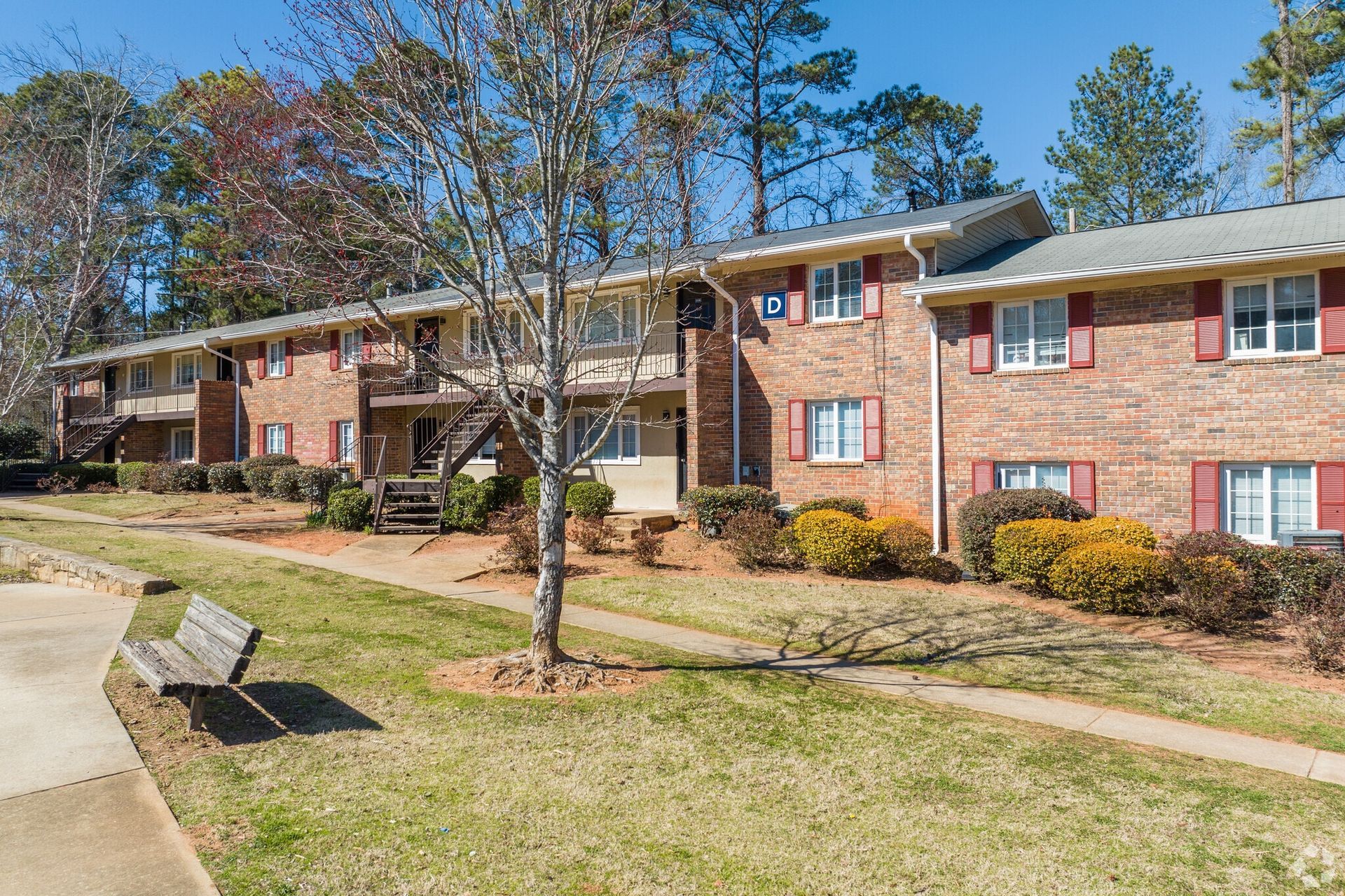 Apartment building with red brick, red shutters, and a bench in front.