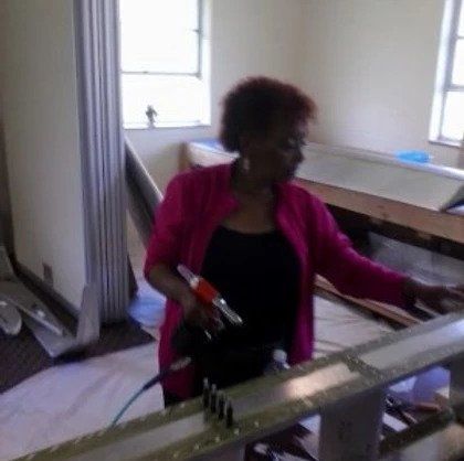 A woman in a pink jacket is standing next to a ladder in a room.