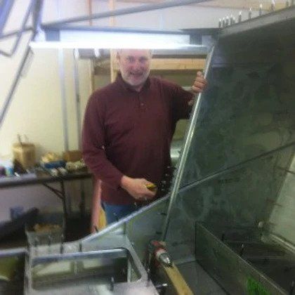 A man in a red shirt is standing in a kitchen holding a screwdriver.