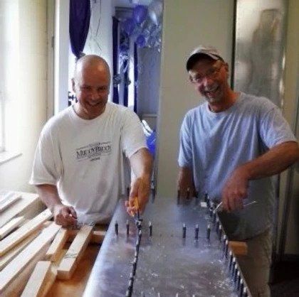 Two men standing next to each other with one wearing a shirt that says miller bros