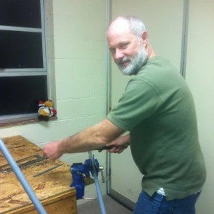 A man in a green shirt is working on a piece of wood