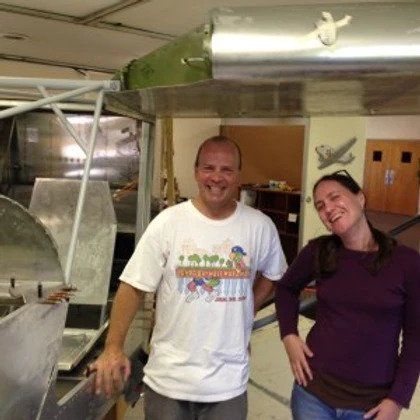 A man and a woman are posing for a picture in front of a plane