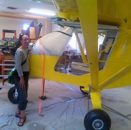 A woman is standing next to a yellow airplane