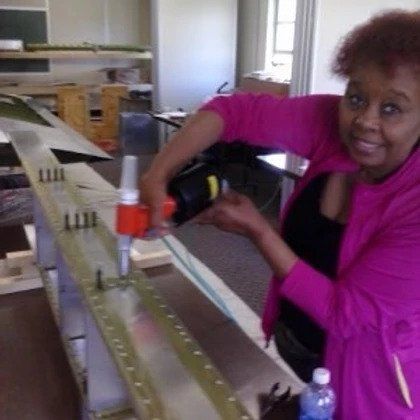 A woman in a pink jacket is working on a piece of metal