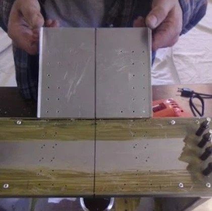 A man is holding a piece of metal over a wooden table.