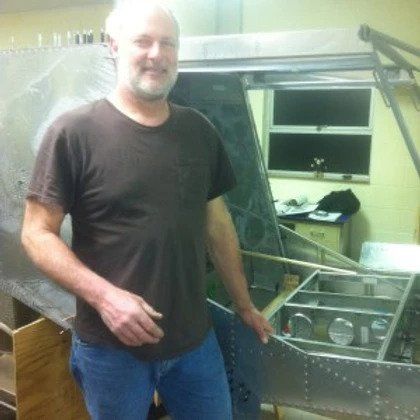 A man in a brown shirt is standing in front of a metal structure