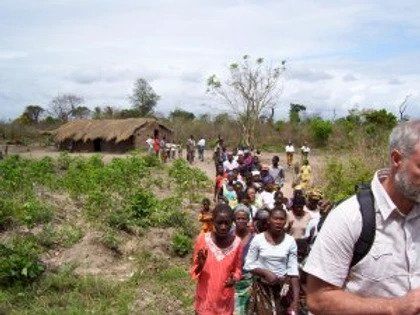 A man with a backpack is standing in front of a group of people in a field.