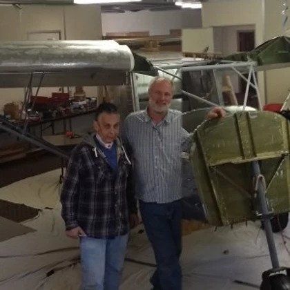 Two men are posing for a picture in front of a plane