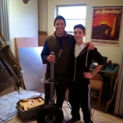 Two men are posing for a picture in front of a poster that says amazing
