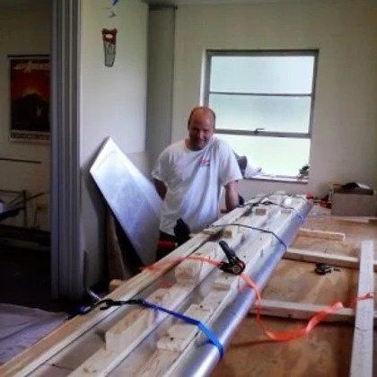 A man in a white shirt is standing next to a large piece of wood