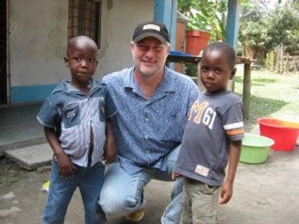A man is posing for a picture with two children one of whom is wearing a shirt that says migi