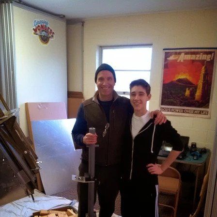 Two men are posing for a picture in front of a poster that says amazing