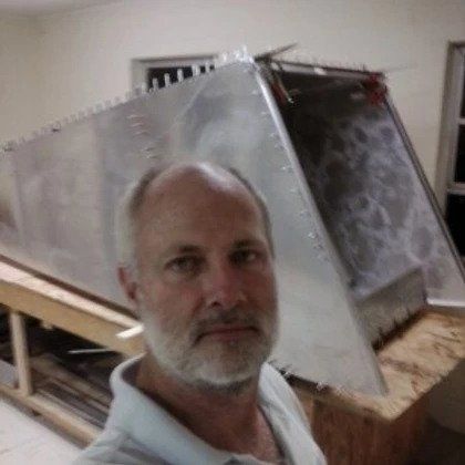 A man with a beard is taking a selfie in front of a large piece of metal.