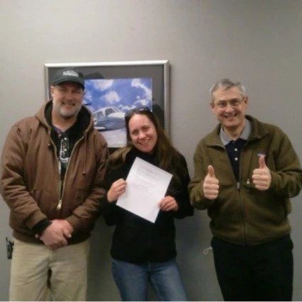 Three people giving a thumbs up in front of a picture