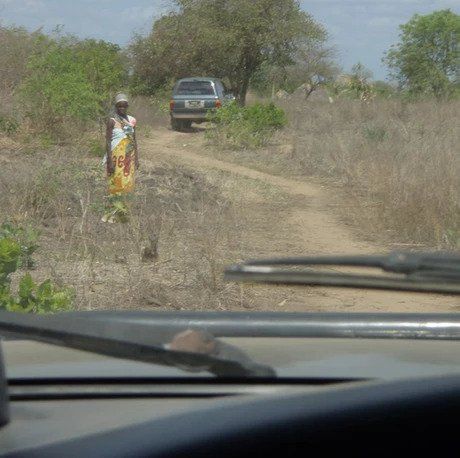 A woman walking down a dirt road with a truck in the background