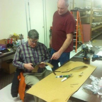 Two men are working on a piece of cardboard