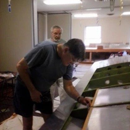 Two men are working on an airplane wing in a room