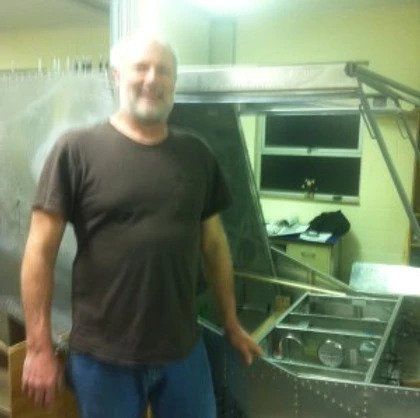 A man in a brown shirt is standing in front of a metal structure
