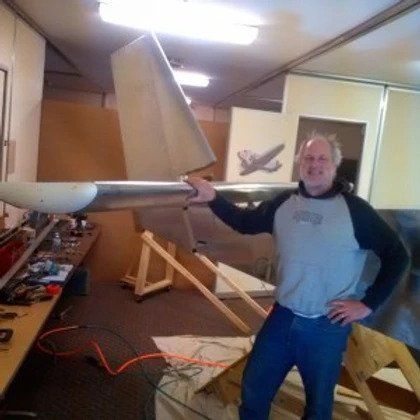 A man is standing in a room holding a large plane wing.