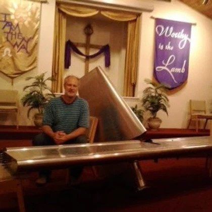 A man sits in front of a sign that says worthy is the lamb