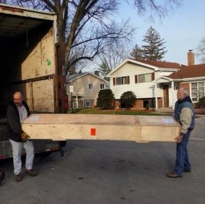 Two men are carrying a large piece of wood in front of a house