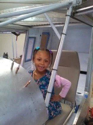 A little girl is sitting in the back seat of a plane.