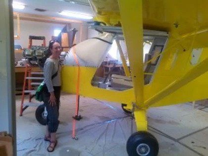 A woman standing next to a yellow airplane in a garage