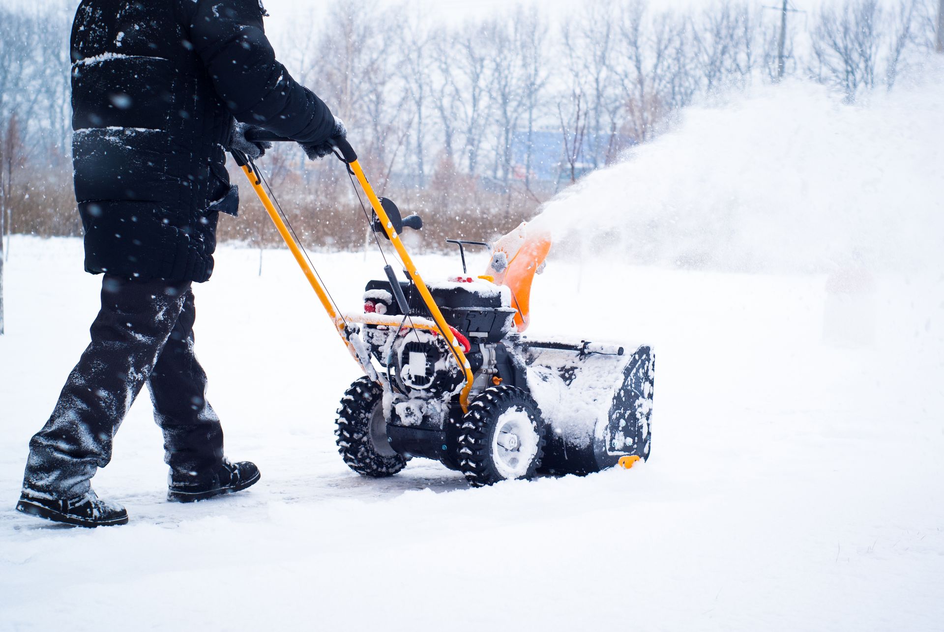 A man operating a snow removal machine clears snow from a sidewalk.