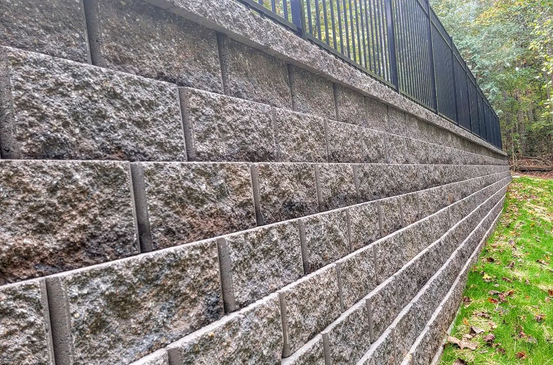 Block retaining wall featuring a sleek black iron fence on top, providing both structural support and a stylish boundary for the property.