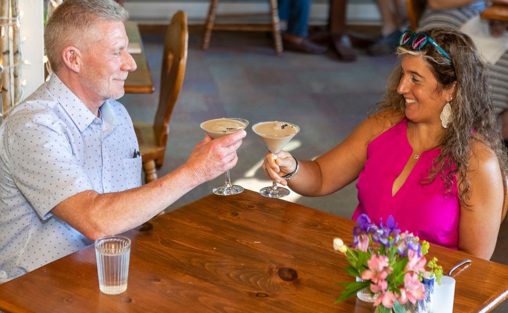 A man and a woman are sitting at a table holding martini glasses.