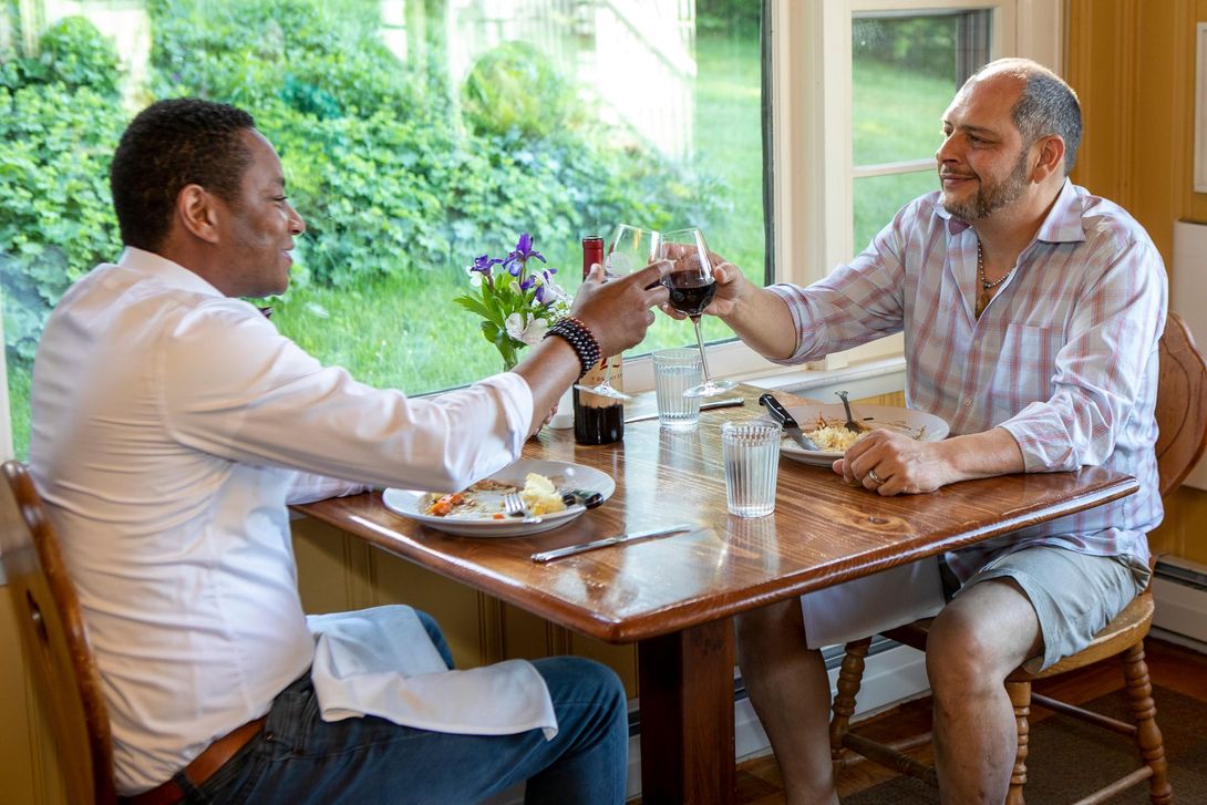 Two men are sitting at a table toasting with wine glasses.