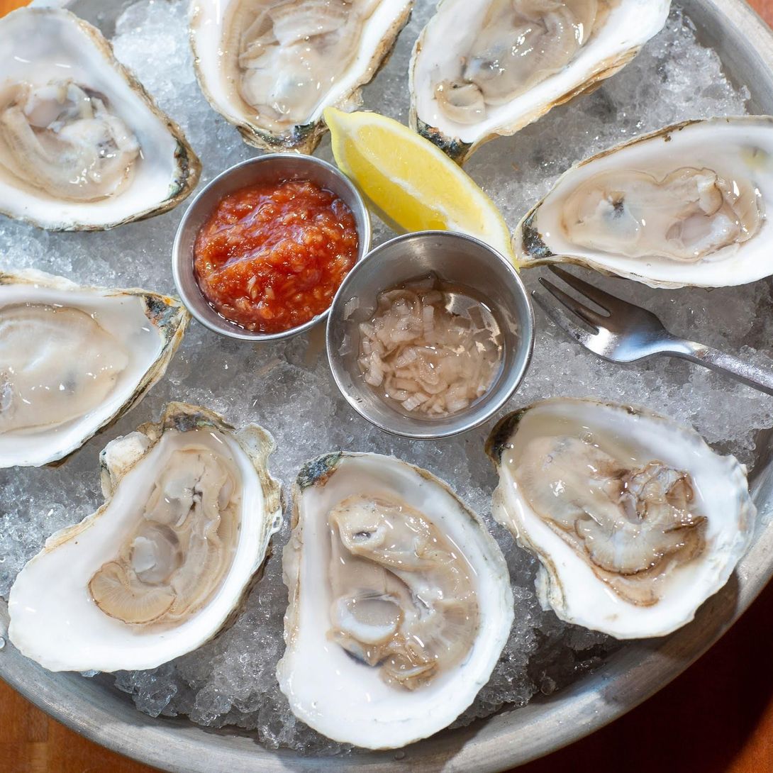 A plate of oysters on ice with sauces and a slice of lemon
