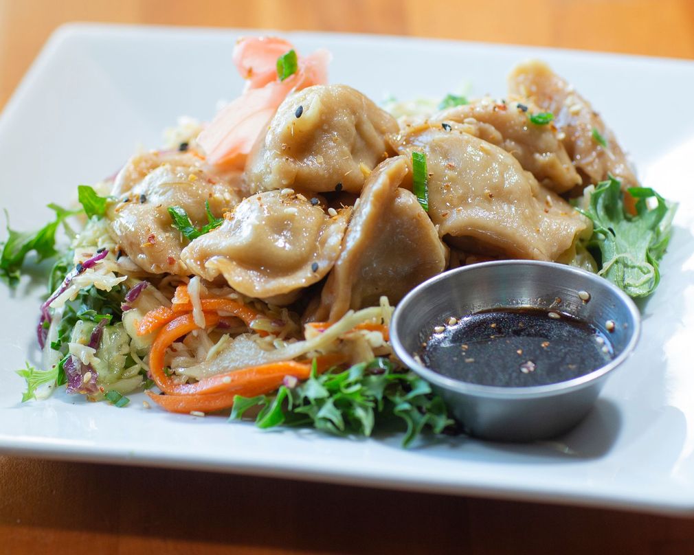 A white plate topped with dumplings and vegetables next to a small bowl of dipping sauce.