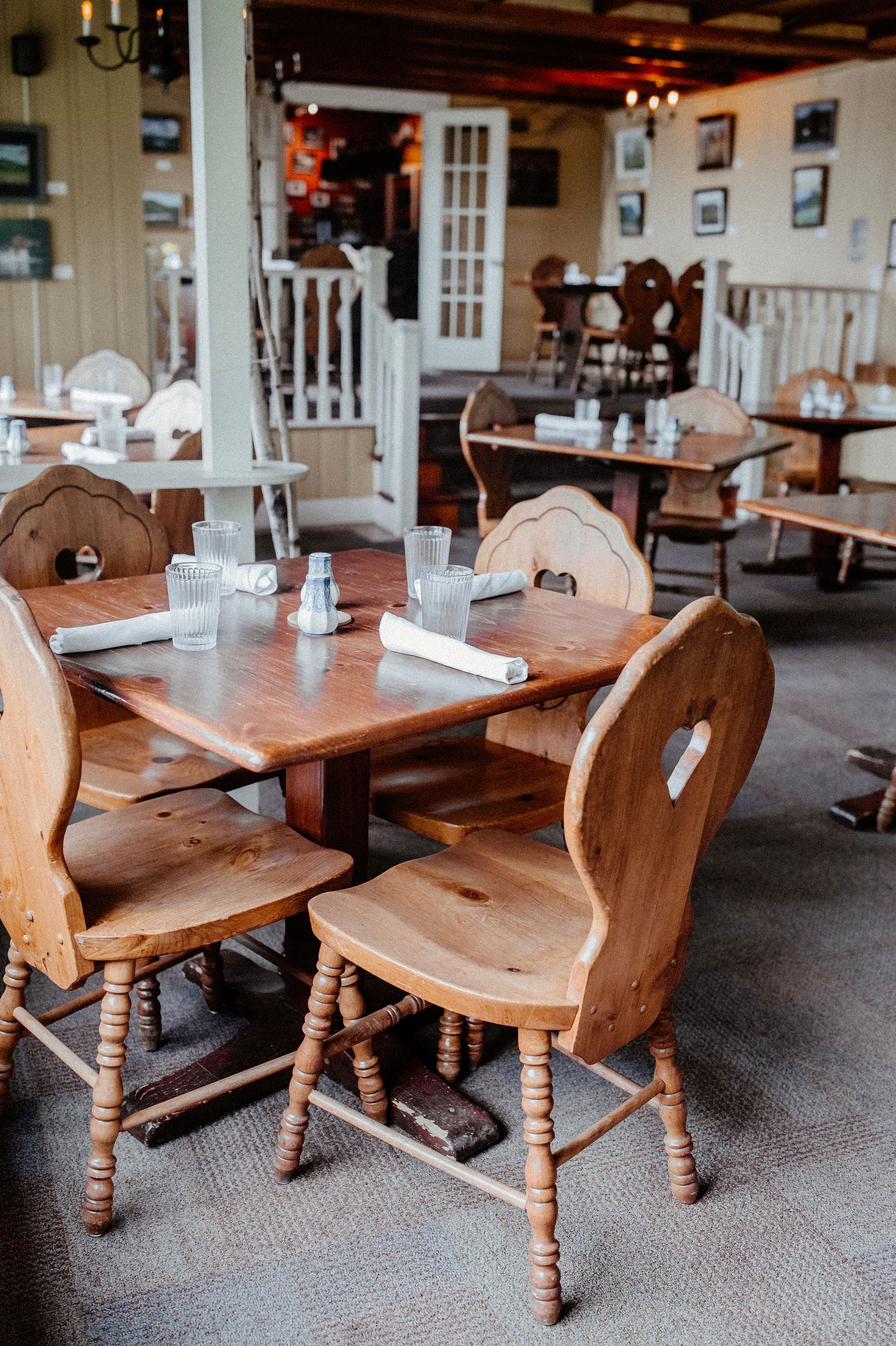 Wooden tables and chairs in a rustic restaurant interior, white door, framed art, and neutral-toned walls.