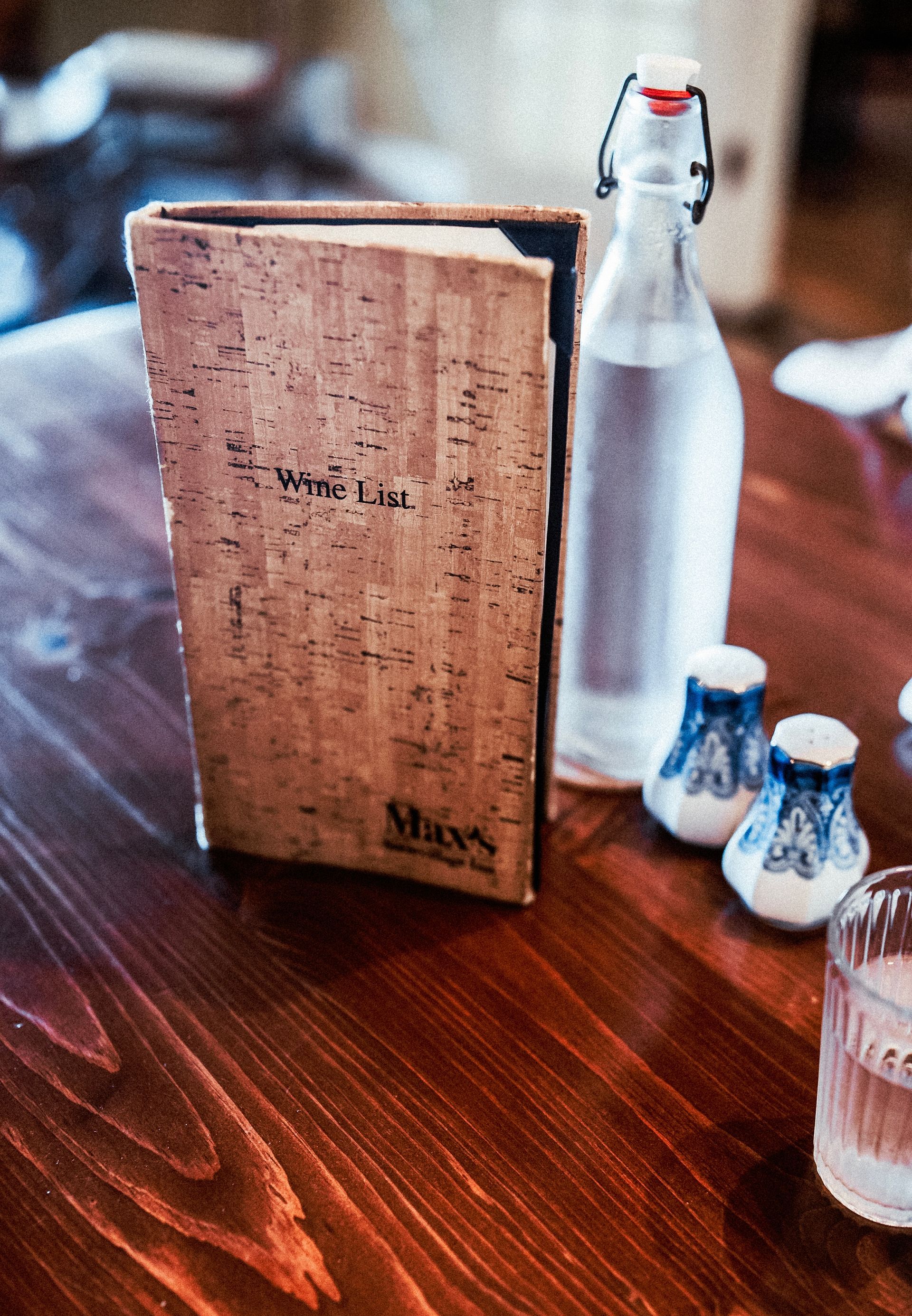 Wooden table setting with menu, water bottle, salt shakers, and a glass of water.