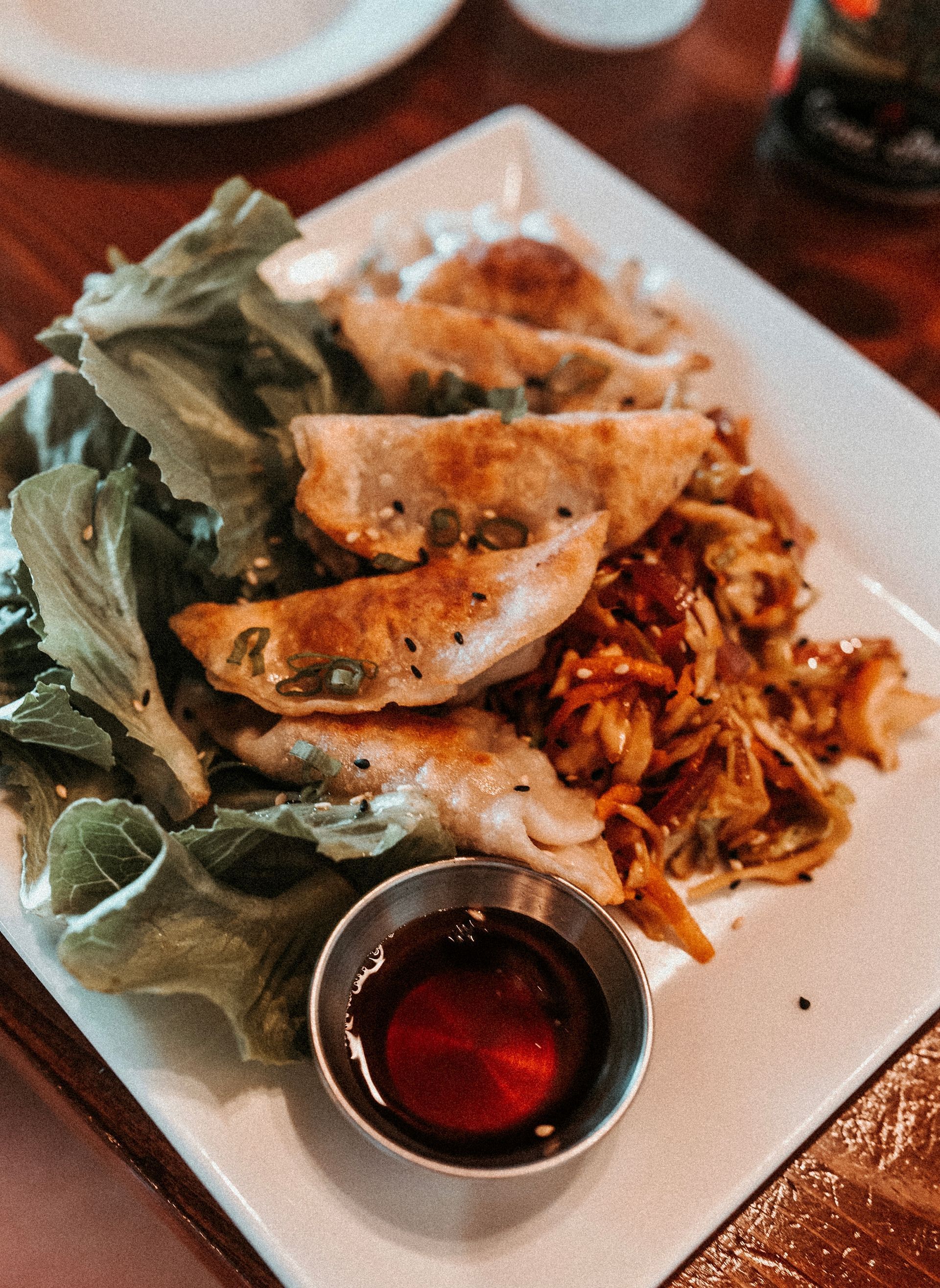Plate of pan-fried dumplings with greens and a side of dipping sauce.
