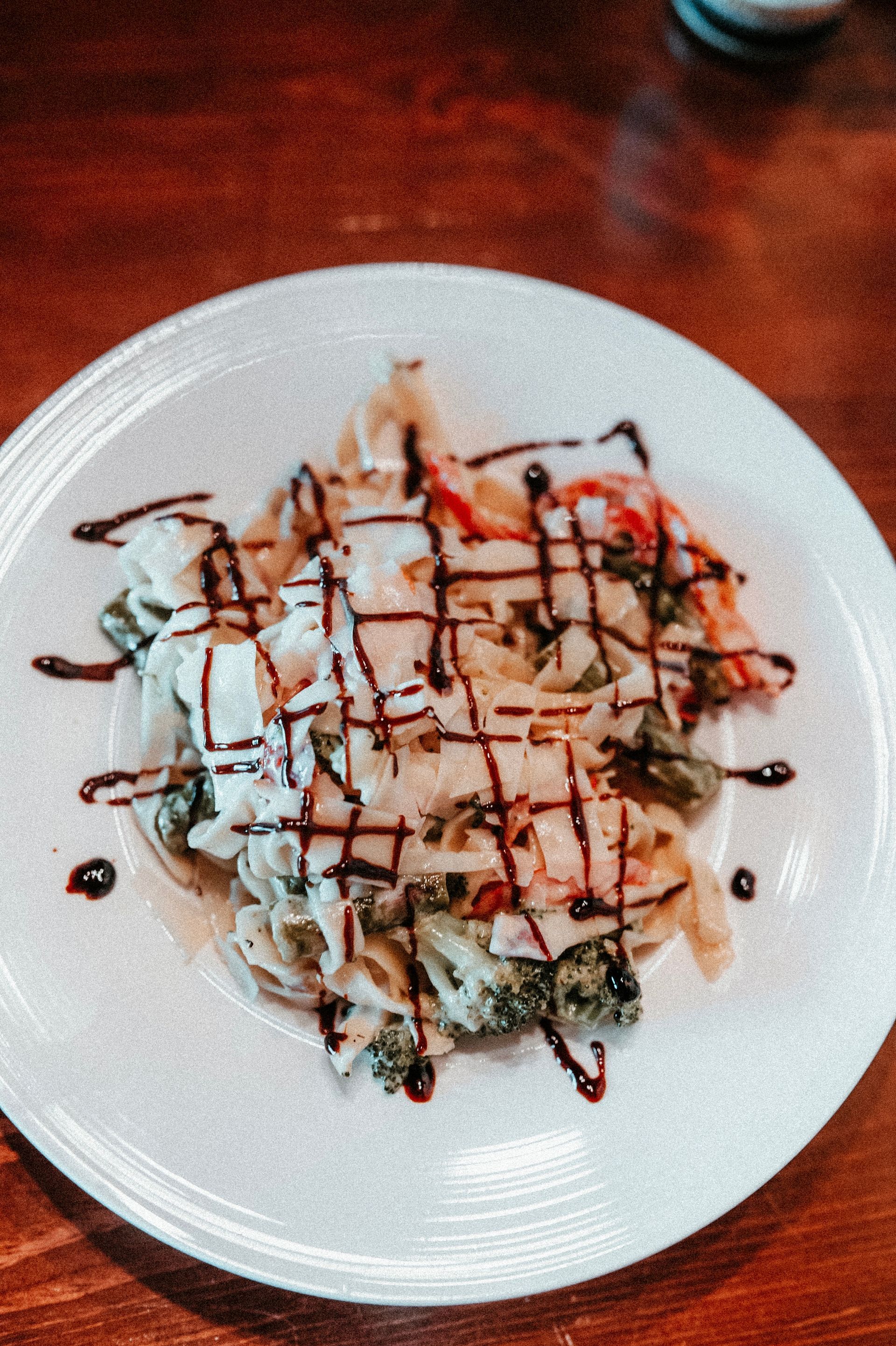 Pasta dish with vegetables, topped with a dark sauce, on a white plate.