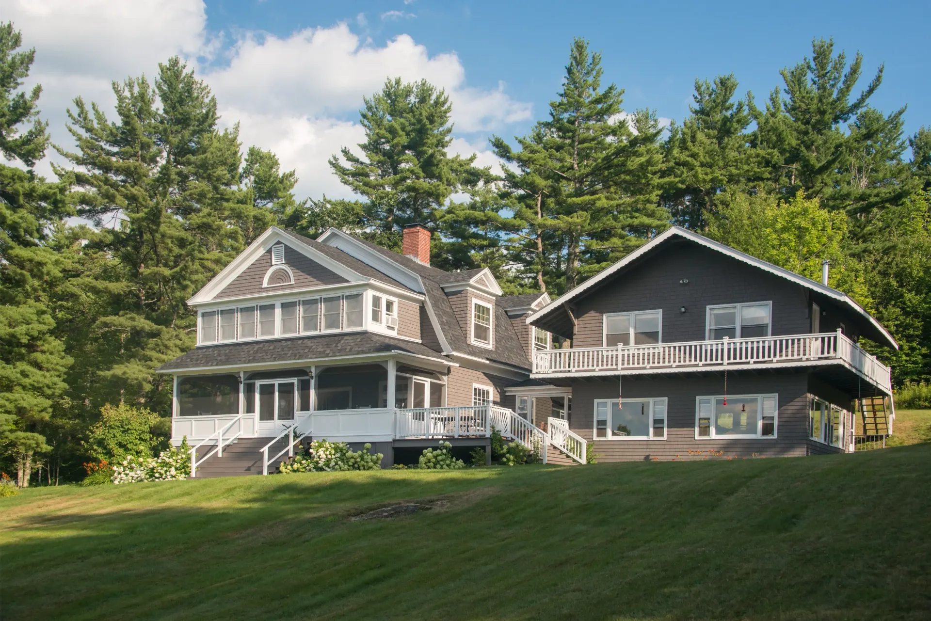 A large house is sitting on top of a lush green hillside surrounded by trees.