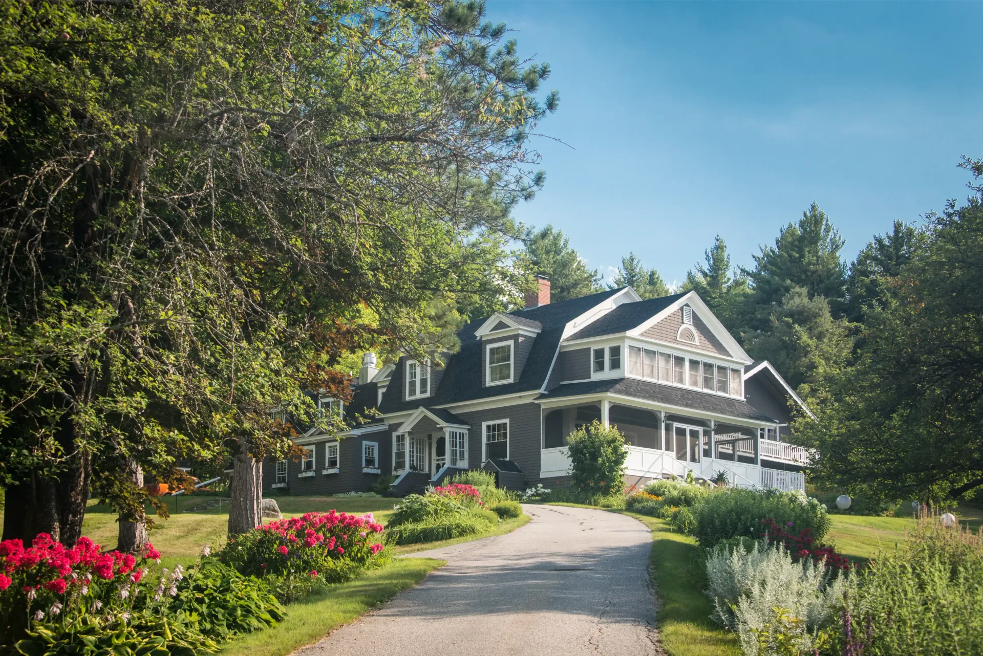 A large house is surrounded by trees and flowers on a sunny day.