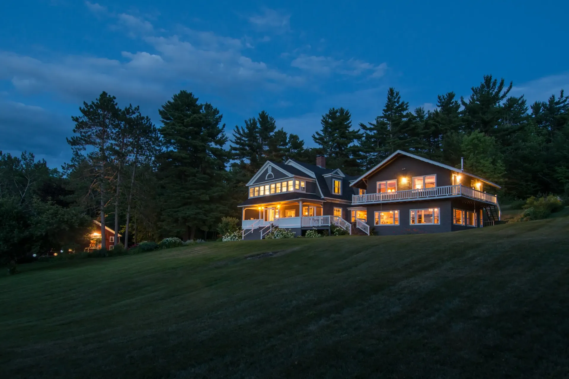 A large house is lit up at night in the middle of a field surrounded by trees.