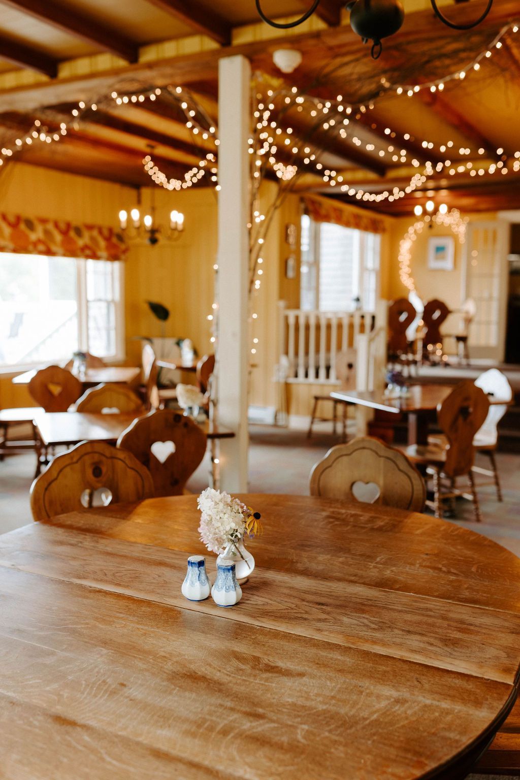 Restaurant interior with wooden tables and chairs, string lights, and a white column.